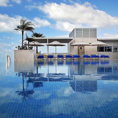 迪拜大都会大酒店 外观 照片 The photo depicts a luxurious swimming pool with a stunning infinity edge. The water is calm and reflects the sky, creating a serene atmosphere. Surrounding the pool are several blue lounge chairs with white umbrellas, providing spots for relaxation.