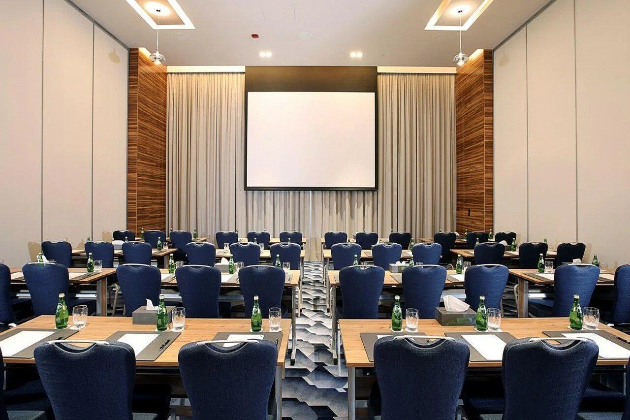 迪拜大都会大酒店 外观 照片 The photo shows a conference room set up for a meeting or presentation. There are several rows of tables arranged in a classroom style, each equipped with blue chairs. On each table, there are notepads and pens, and bottles of water are available for