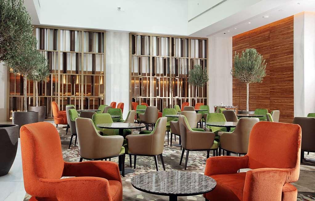 迪拜大都会大酒店 餐厅 照片 The photo shows a modern, stylish lounge area with comfortable seating. The space features multiple tables surrounded by chairs in vibrant colors, including orange and green. There are also decorative plants in the corners, adding a touch of greenery
