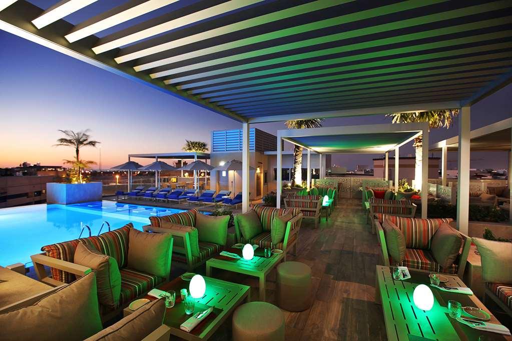 迪拜大都会大酒店 设施 照片 The photo shows a stylish outdoor lounge area, likely at a hotel or resort. There are comfortable seating arrangements with striped cushions and small tables, illuminated with soft green lights. In the background, there is a swimming pool with lounge