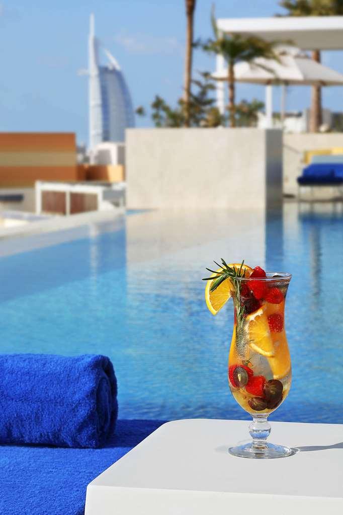 迪拜大都会大酒店 设施 照片 The photo shows a refreshing cocktail placed on the edge of a pool. The drink is garnished with slices of lemon, raspberries, and possibly some herbs, and is served in a tall glass. In the background, there is a clear blue water surface of the pool, 