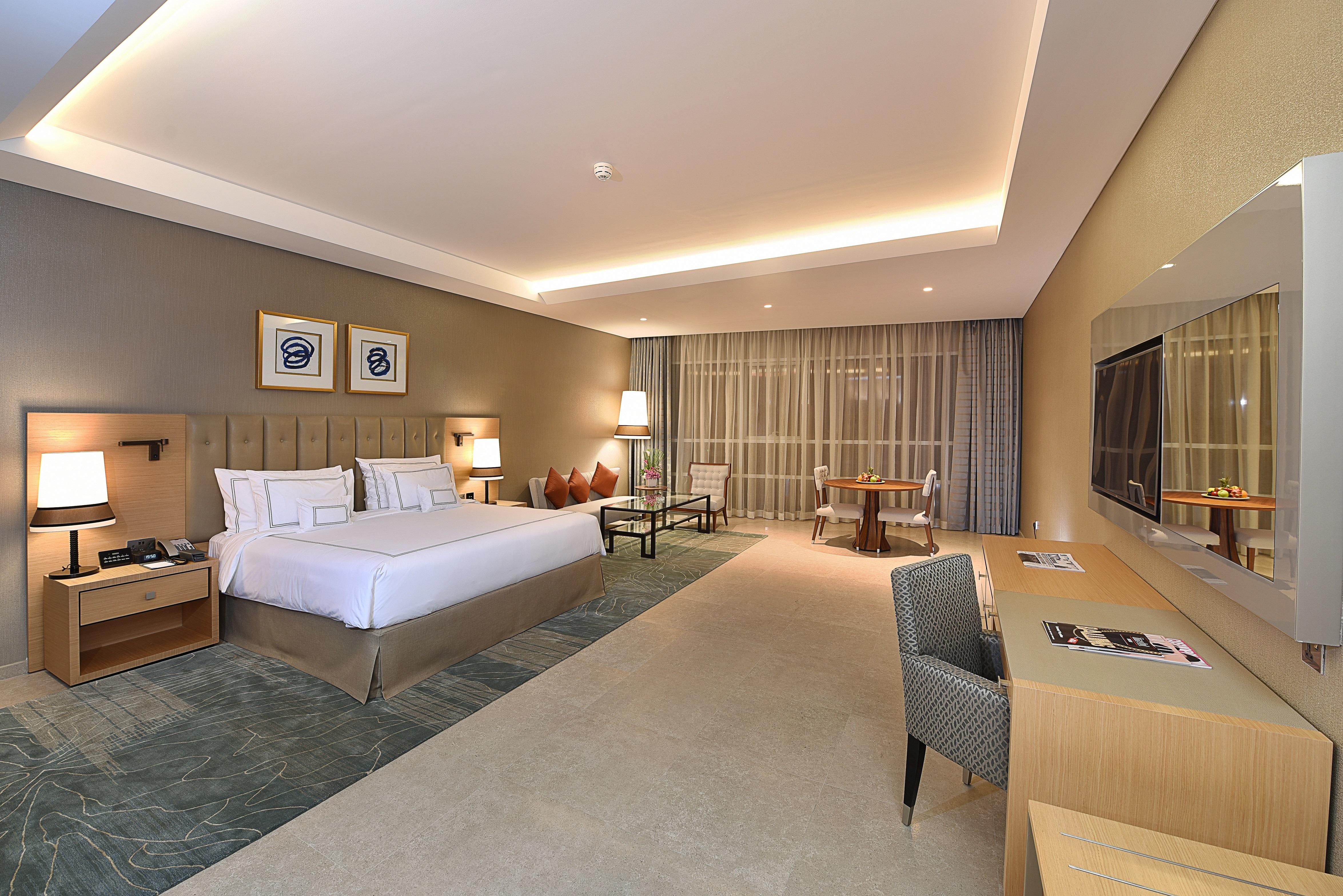 迪拜大都会大酒店 外观 照片 The photo shows a modern hotel room. It features a spacious layout with a large bed, complemented by bedside tables and lamps. There's a comfortable seating area with two chairs and a small table. A desk with a chair is positioned against one wall, a