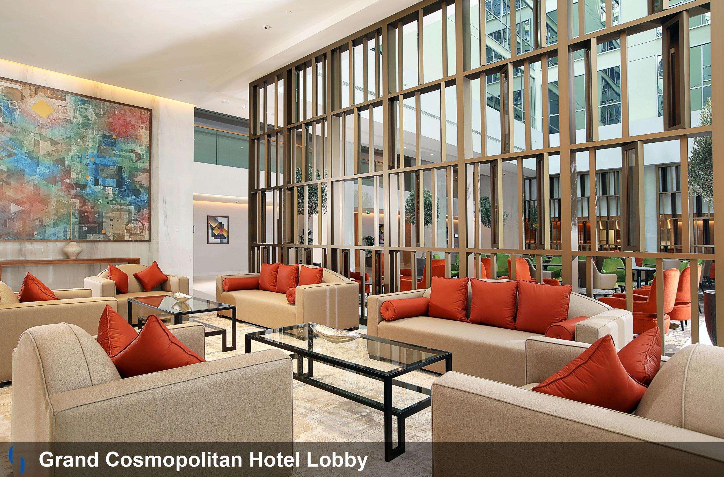 迪拜大都会大酒店 外观 照片 The image shows the lobby of the Grand Cosmopolitan Hotel. The space features a modern and stylish design, with beige sofas and bright orange cushions arranged around glass coffee tables. There are decorative elements such as a large abstract paintin