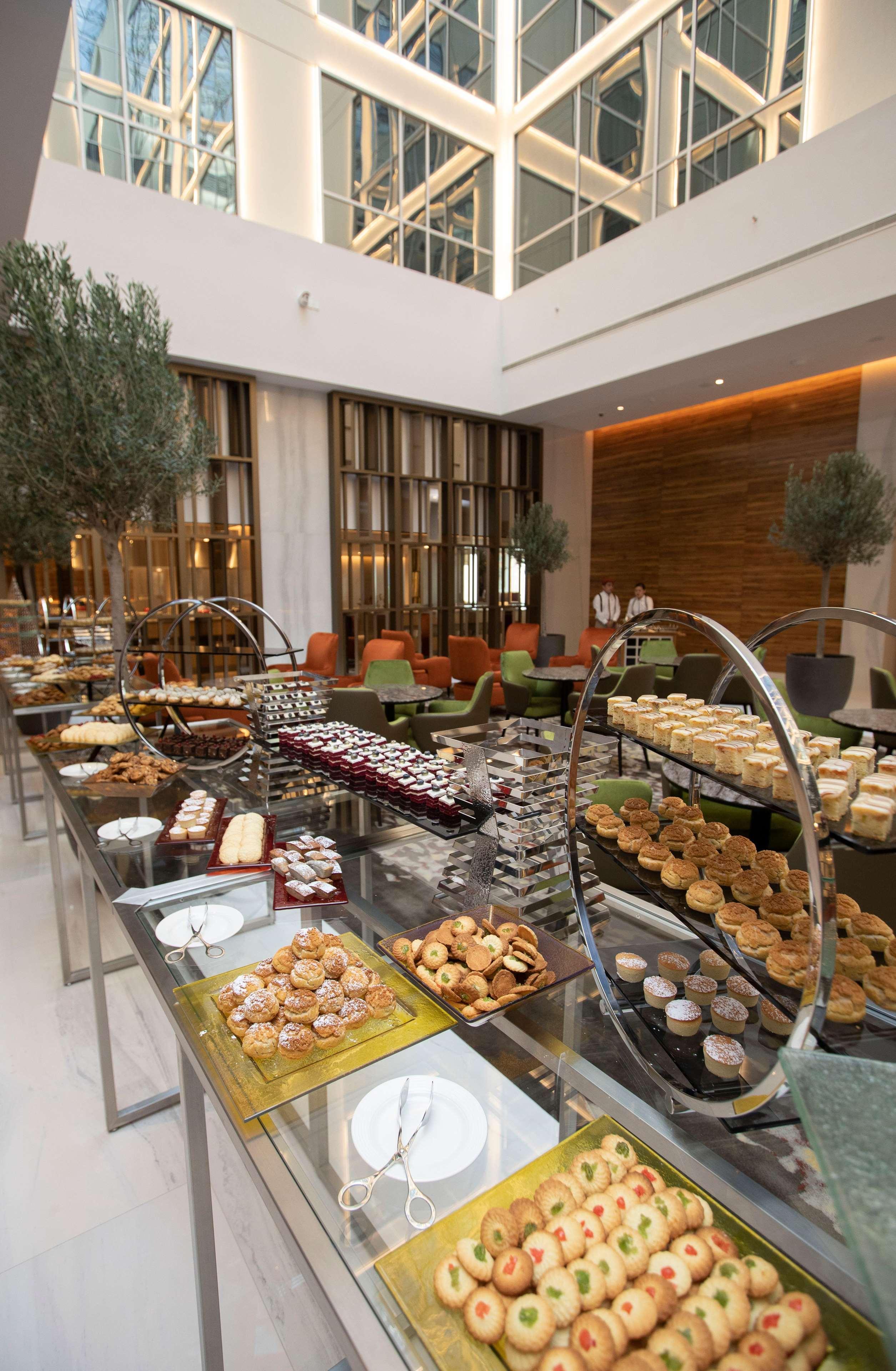 迪拜大都会大酒店 外观 照片 The photo depicts a beautifully arranged dessert buffet in a modern setting. Various types of pastries and sweets are displayed on elegant stands and tables. You can see an assortment of items, including cakes, tarts, cookies, and small desserts, app