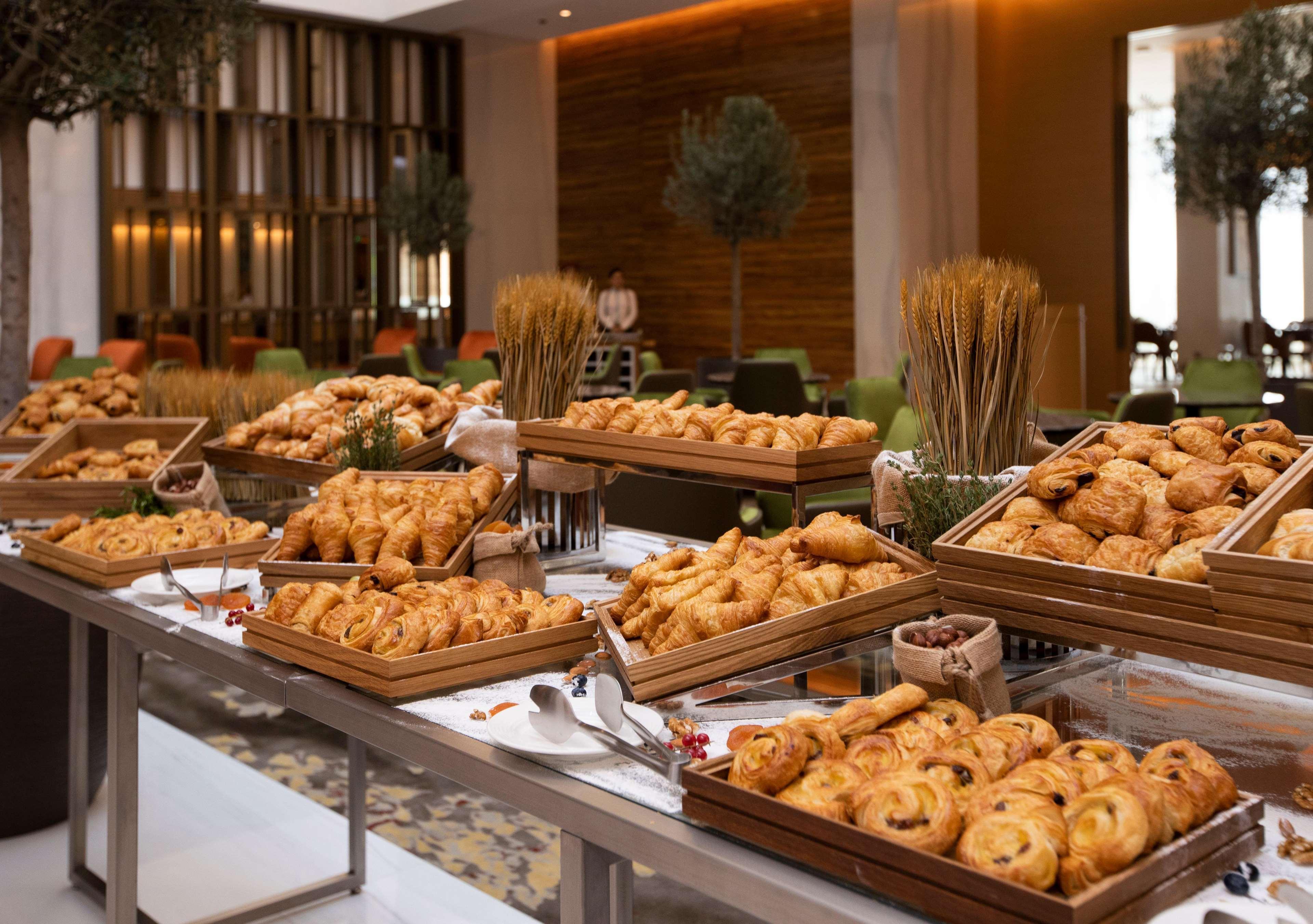 迪拜大都会大酒店 外观 照片 The photo shows a lavish spread of baked goods laid out on a table in a buffet setting. There are various trays filled with an assortment of pastries, including croissants, danishes, and other types of bread. The presentation is appealing, with the p
