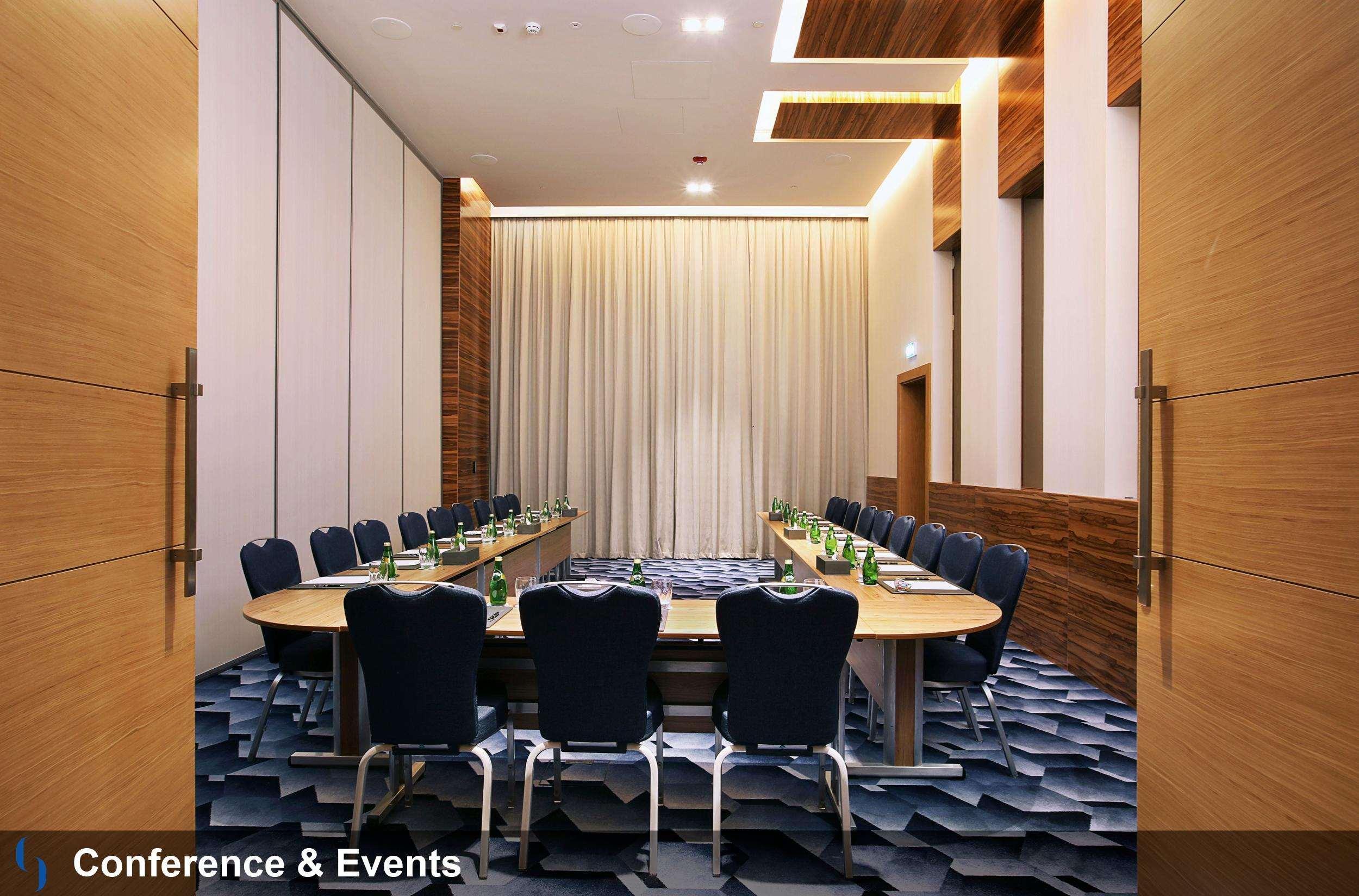 迪拜大都会大酒店 外观 照片 The photo shows an elegantly designed conference room. It features a large, rectangular table surrounded by ergonomic chairs, primarily in a dark blue color. The room has wooden accents on the walls, paired with light-colored curtains. The flooring a