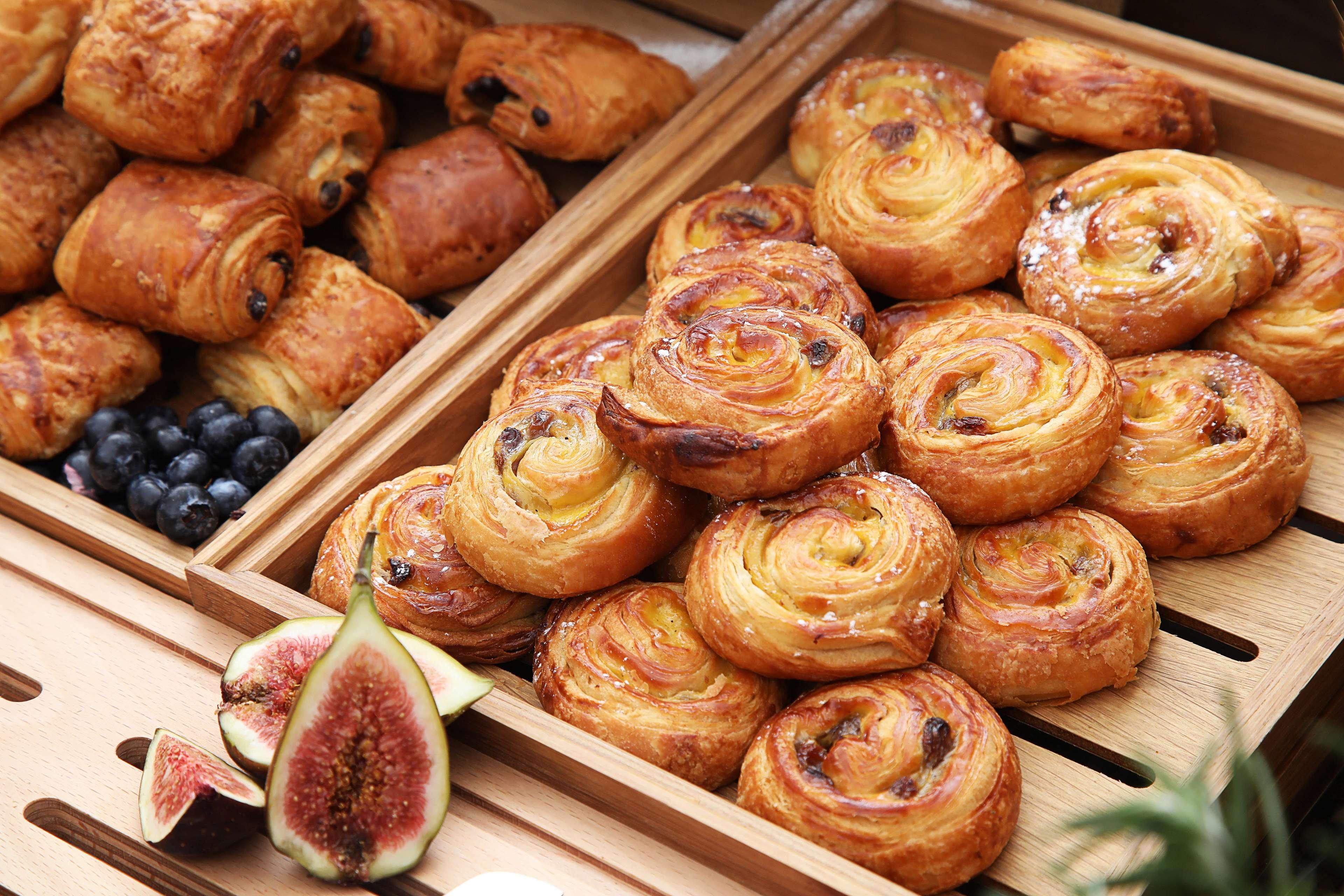 迪拜大都会大酒店 外观 照片 The photo showcases a selection of baked goods, primarily featuring various types of pastries. In one wooden tray, there are spiral-shaped pastries, likely danishes or cinnamon rolls, characterized by a golden-brown color and a flaky texture. Some of