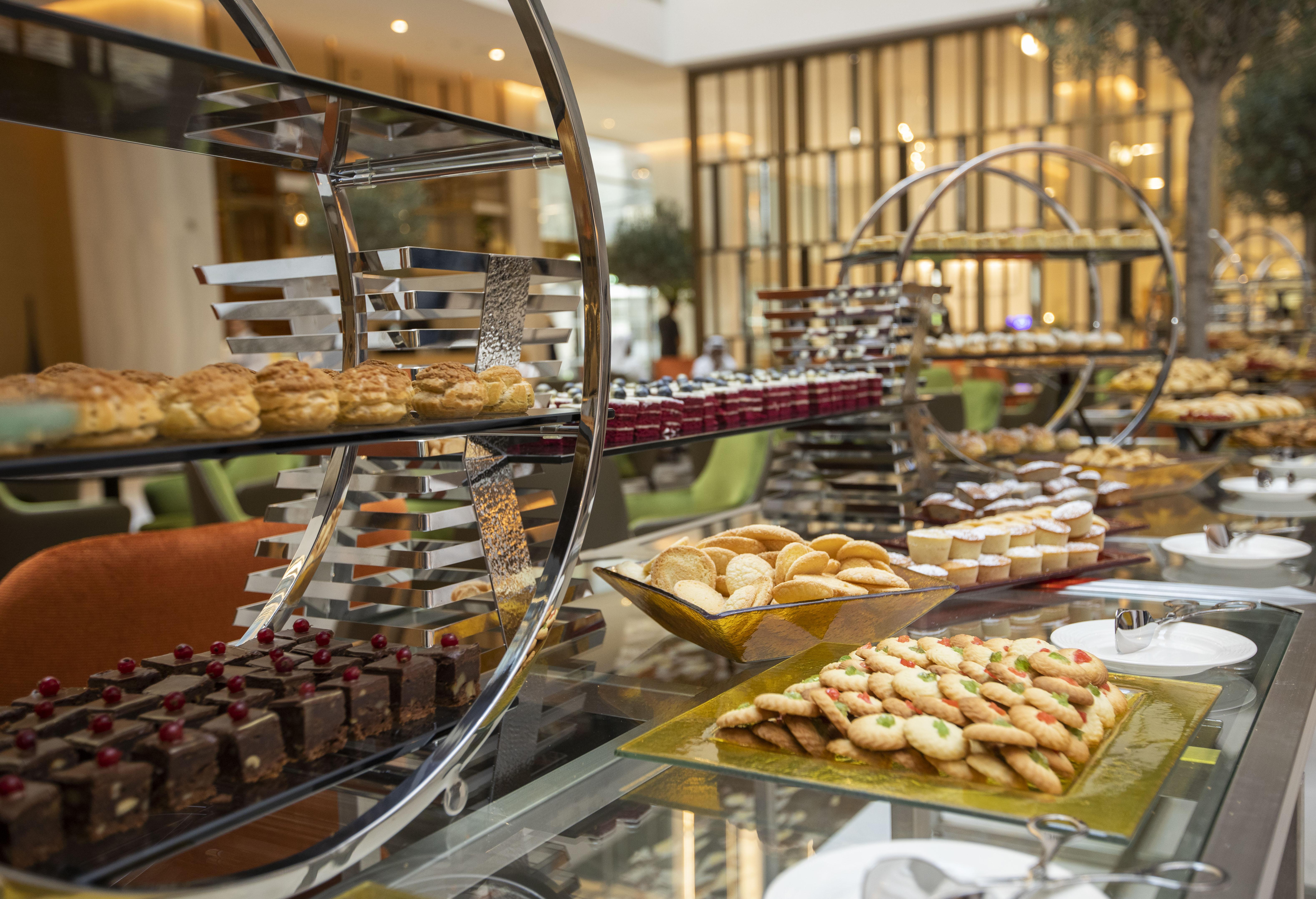 迪拜大都会大酒店 外观 照片 The photo showcases an elegant dessert display featuring a variety of baked goods. There are multiple tiers of treats, including pastries, cookies, and chocolates. On the lower tier, there appears to be an assortment of cookies arranged on a rectangu