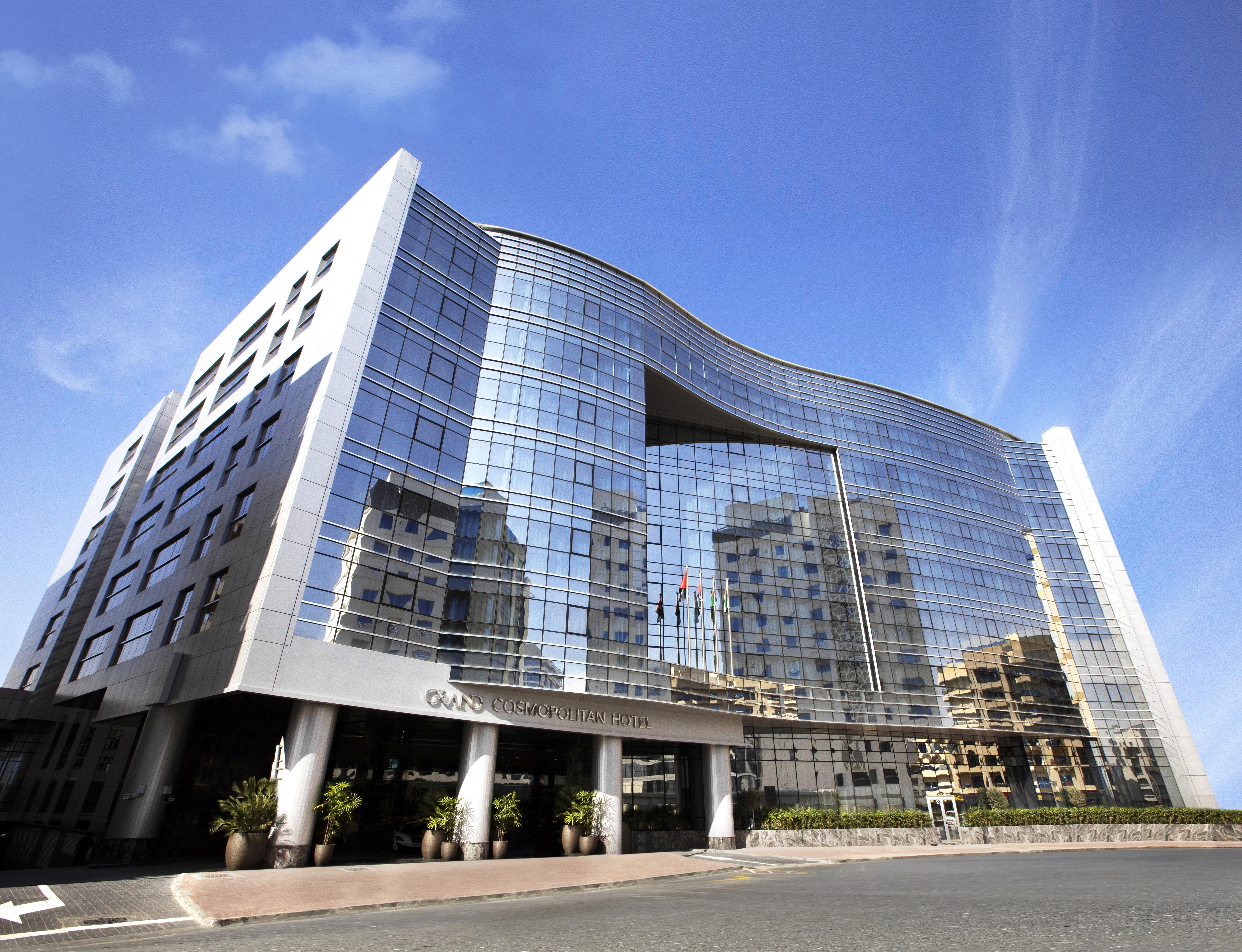 迪拜大都会大酒店 外观 照片 The image shows a modern building with a distinctive architectural design. The facade is predominantly made of glass, reflecting the blue sky and surrounding structures. The building has a curved top, creating a unique silhouette, and is likely multi