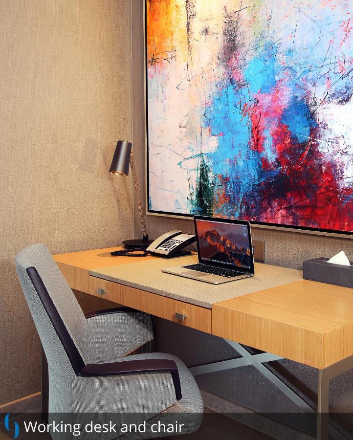 迪拜大都会大酒店 外观 照片 The photo depicts a modern workspace. There's a wooden desk with a sleek design, equipped with a laptop open on the surface. Next to the laptop, there is a classic telephone and a small box of tissues. A stylish lamp is positioned on the desk for lig