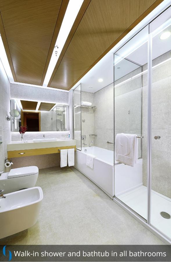 迪拜大都会大酒店 外观 照片 The photo shows a modern bathroom featuring a glass-enclosed shower and a bathtub. The walls are light-colored, creating a clean and spacious feel. A sleek vanity with a sink is integrated into the design, and there are two towels hanging near the ba