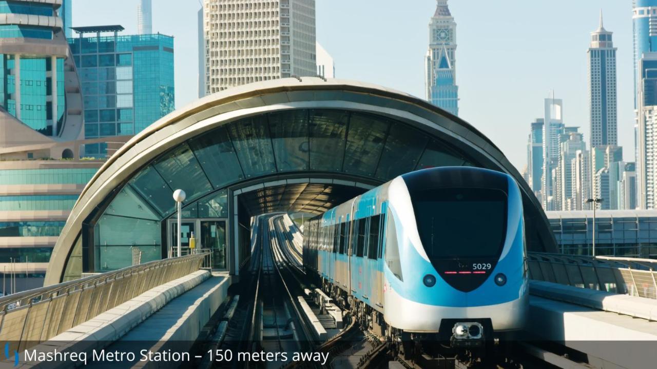 迪拜大都会大酒店 外观 照片 The photo shows a modern metro train approaching a station, with a distinctive curved structure overhead that forms part of the station's design. The scene appears to be set in a city with tall skyscrapers in the background, indicating an urban envir