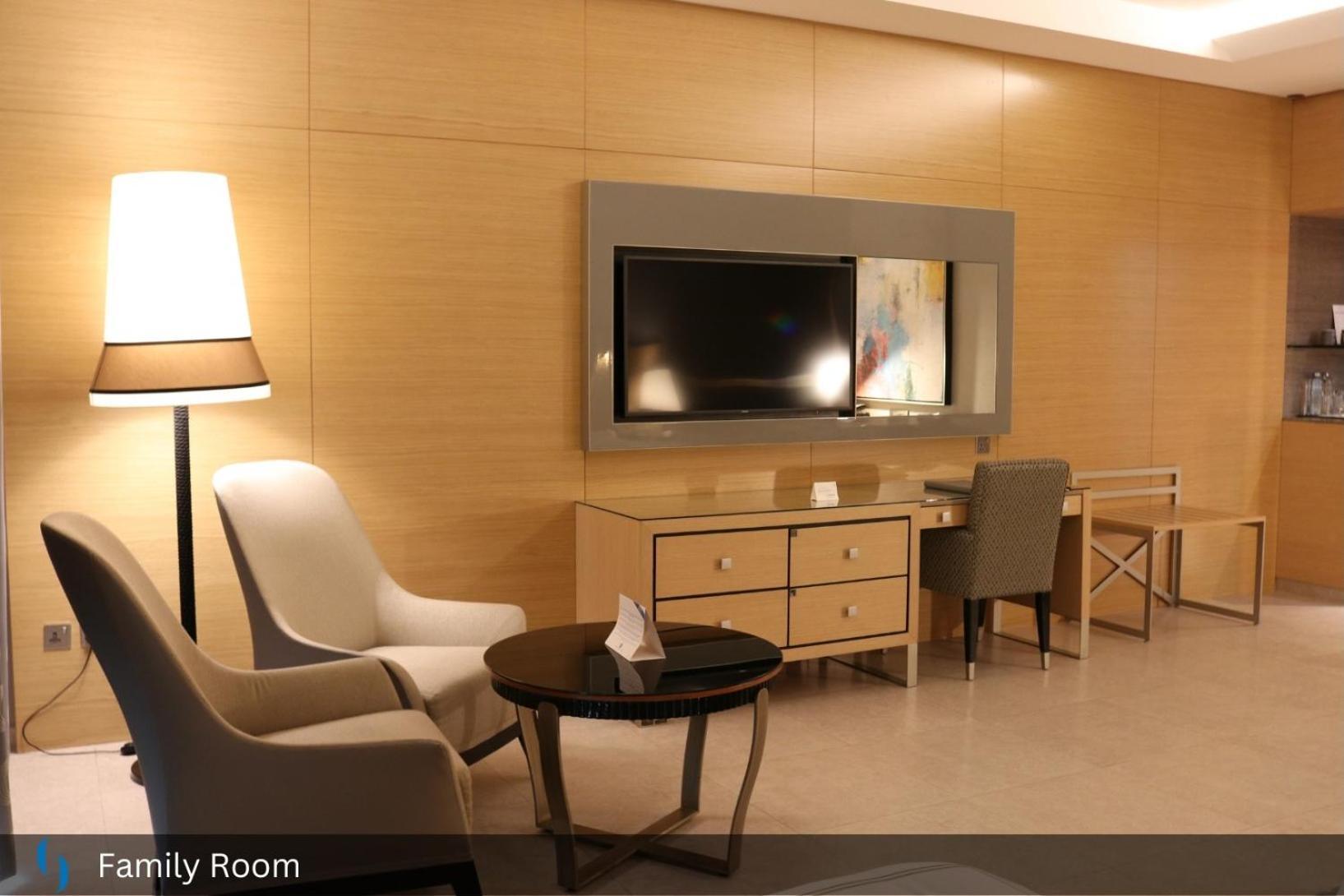 迪拜大都会大酒店 外观 照片 The photo shows a modern family room with a warm and inviting atmosphere. It features a light wood-paneled wall and contains several pieces of furniture:

- A flat-screen television mounted on the wall, positioned above a wooden media console with dr
