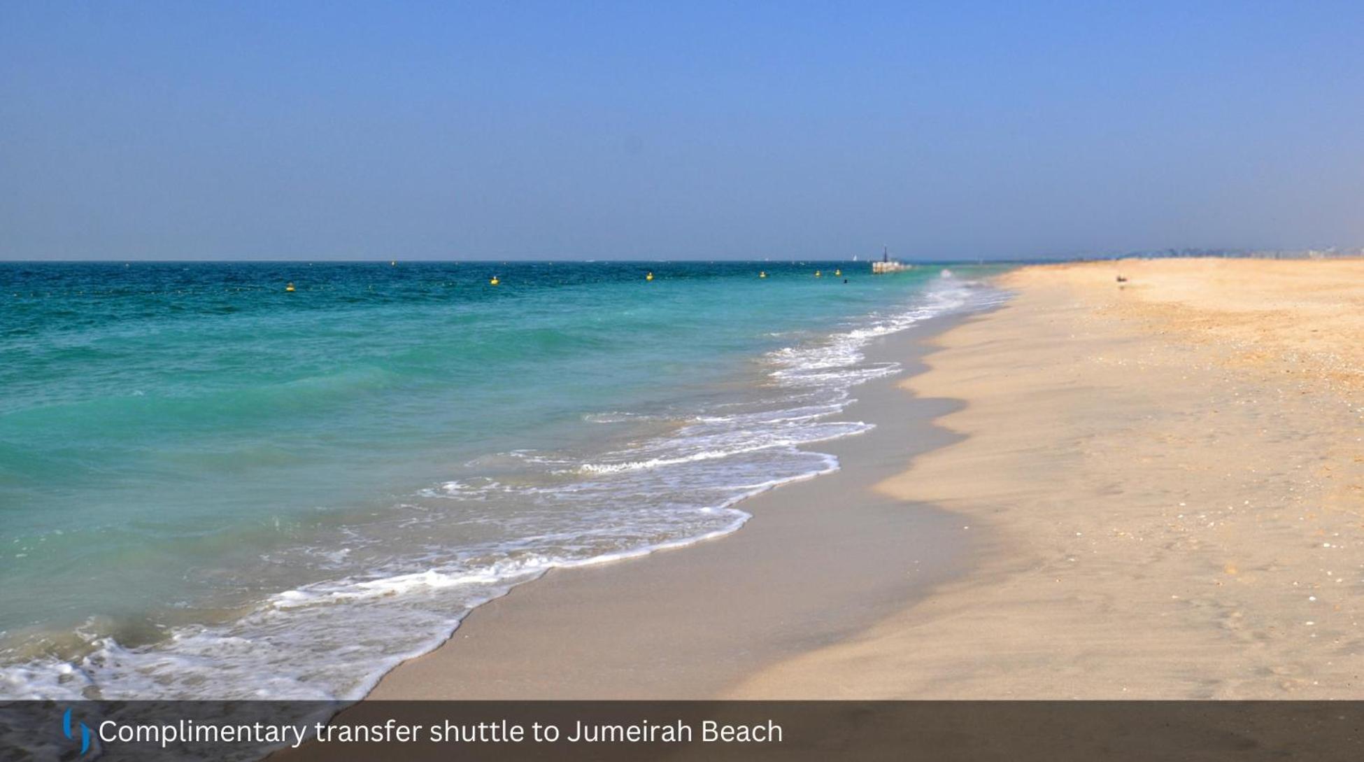 迪拜大都会大酒店 外观 照片 The photo depicts a serene beach scene featuring soft, golden sand and clear turquoise waters. Gentle waves are lapping at the shore, creating a peaceful ambiance. The sky above is mostly clear, suggesting a bright and sunny day. There are some buoys
