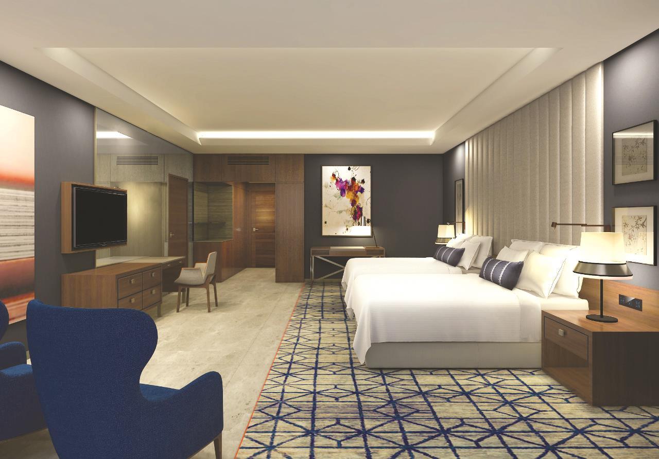 迪拜大都会大酒店 外观 照片 The image shows a modern hotel room featuring two beds with white linens. The room has a sleek design with a combination of blue, gray, and wooden accents. There is a large flat-screen TV mounted on the wall across from the beds. A blue armchair is p