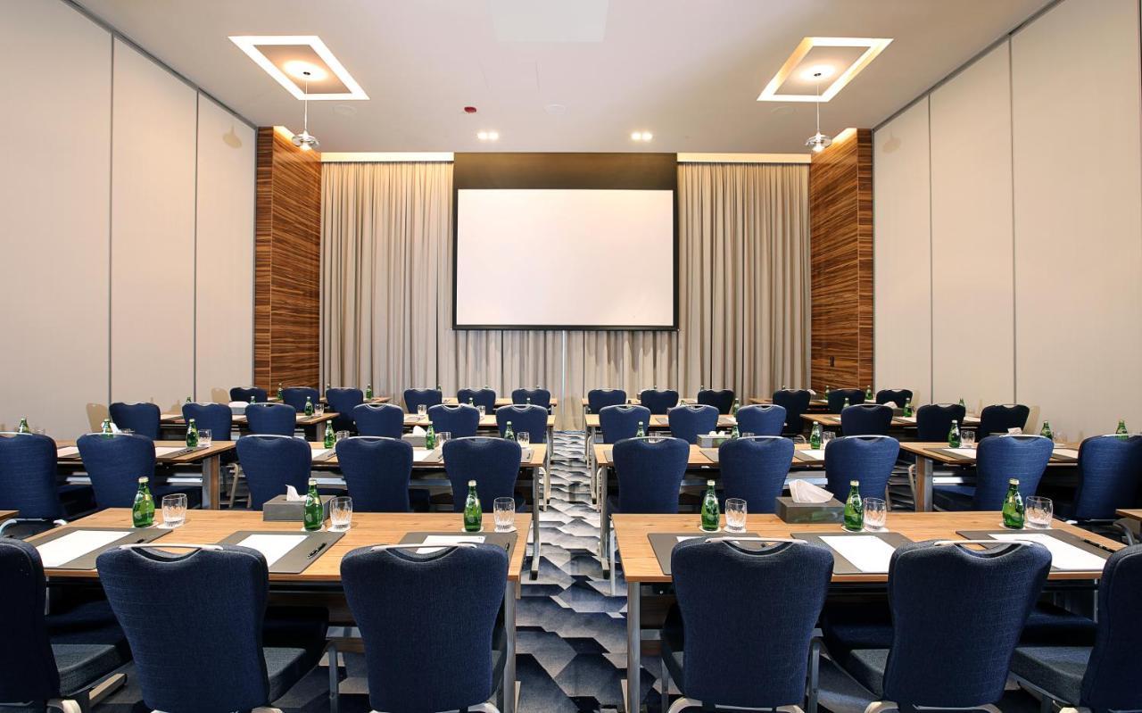 迪拜大都会大酒店 外观 照片 The photo shows a conference room set up for a meeting or presentation. There are several rows of tables arranged in a classroom style, each with blue chairs. Each table appears to have a notepad and pen for participants. At the front of the room, th